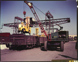 Lowering of industrial vehicle with mobile crane onto railway wagon.