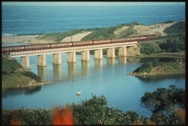 Passenger train on concrete bridge close to shoreline.